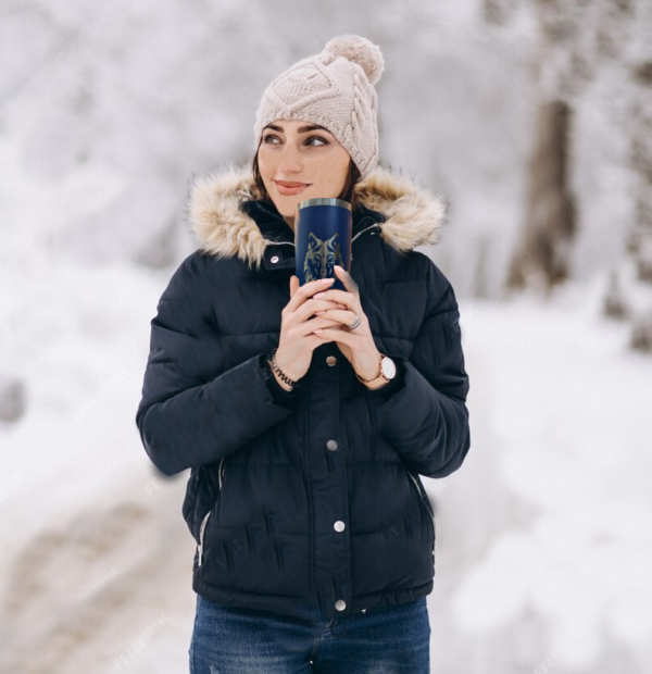 A Girl outside in the cold with snow on the ground holding a blue mug with the engraving of a wolf