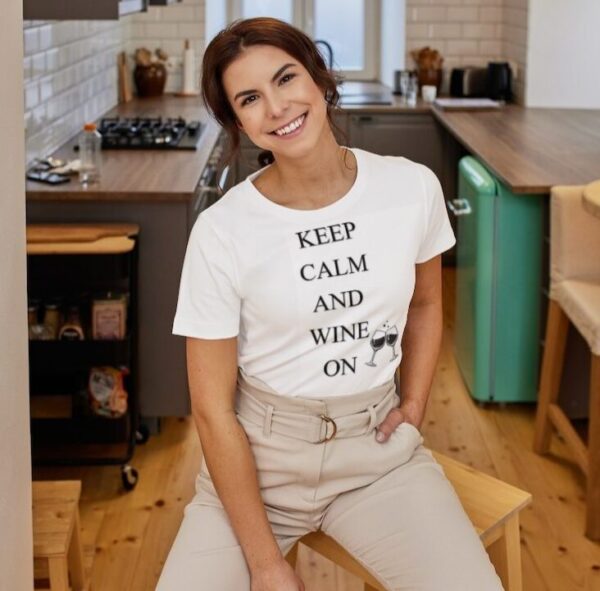 A girl wearing a white T-shirt with writing that says "Keep Calm and Wine On" vertically and two glasses of wine next to "wine and on "